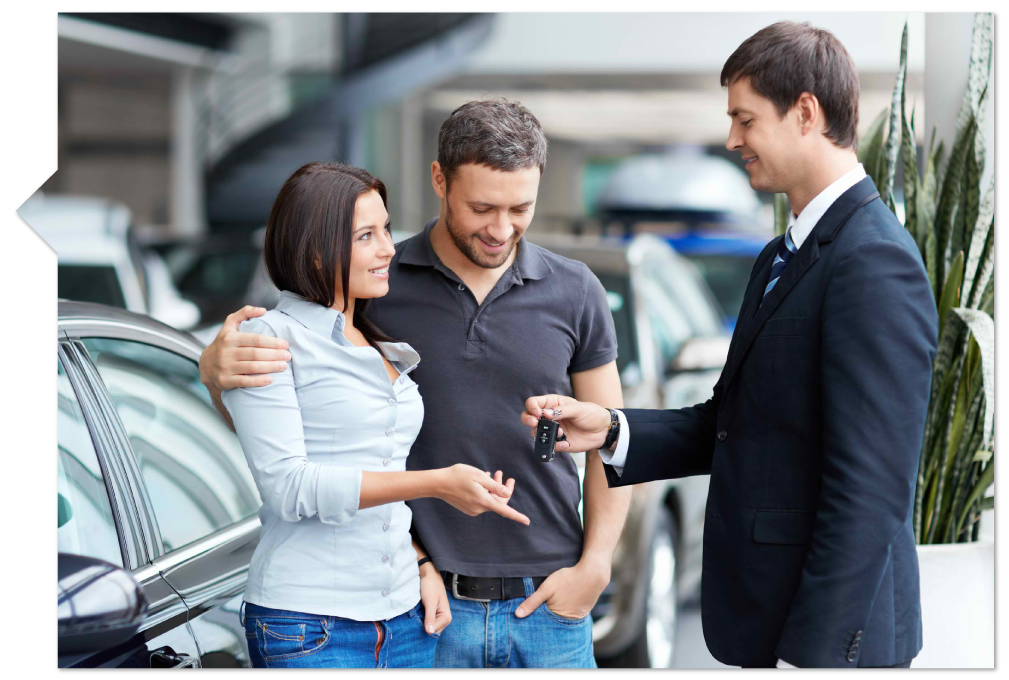 a salesman hands keys to a new car to a couple